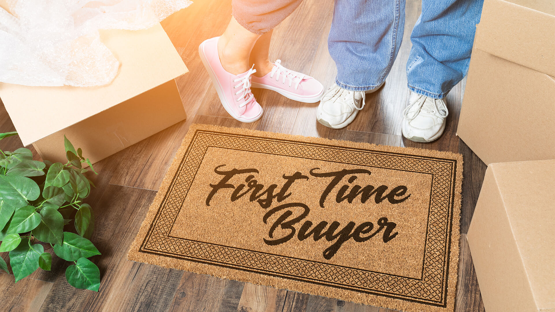 Close up of a welcome mat that reads "first time buyer" with two people's feet above it.