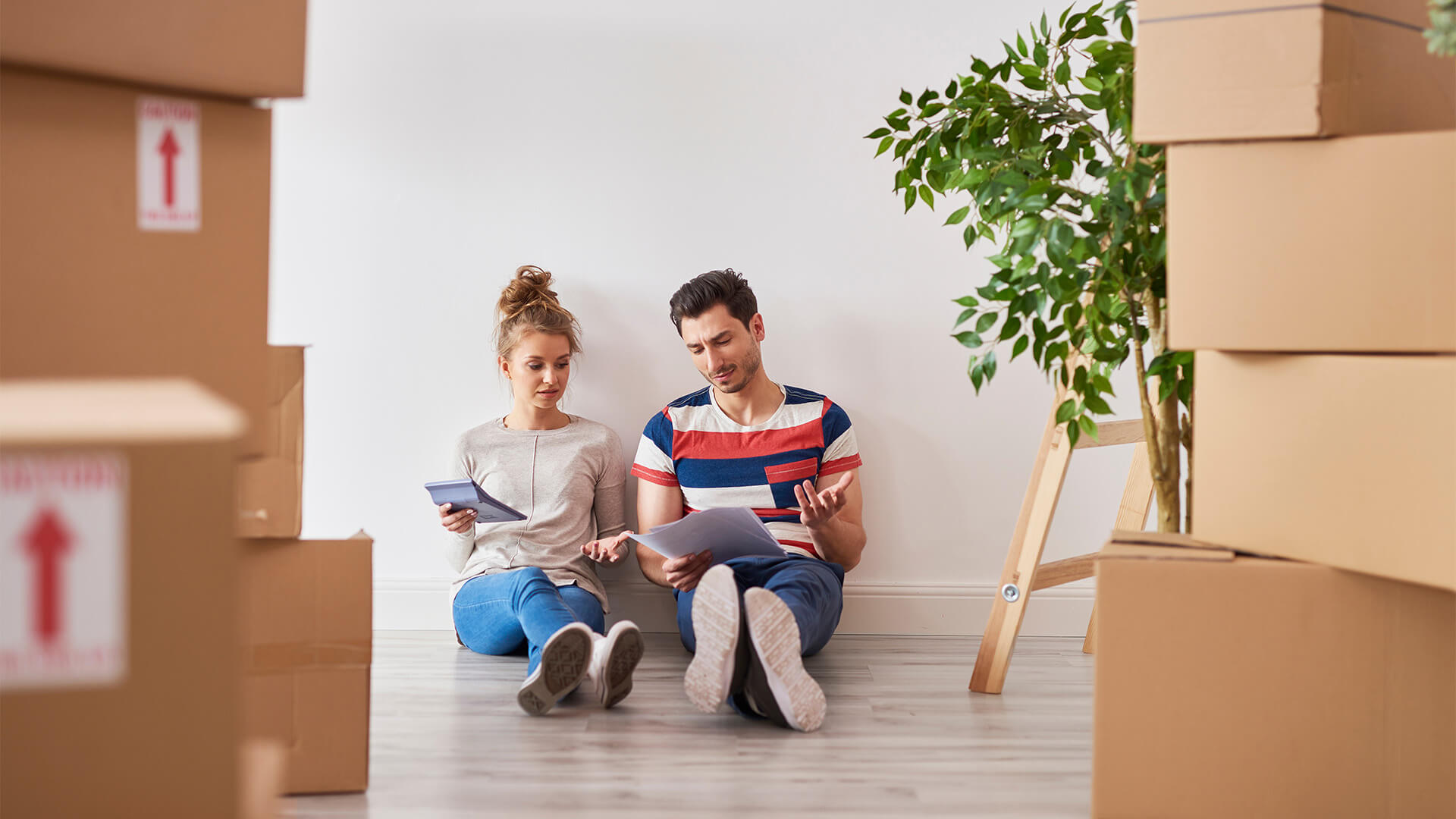 Couple moving out of their home, and sitting on the floor together working on their finances